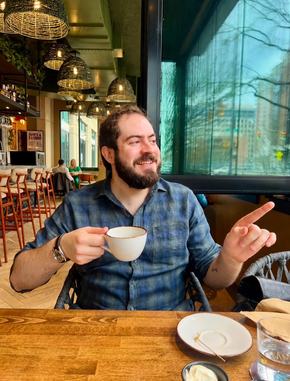 Tyler at a café table, coffee in hand, smiling and pointing mid-conversation