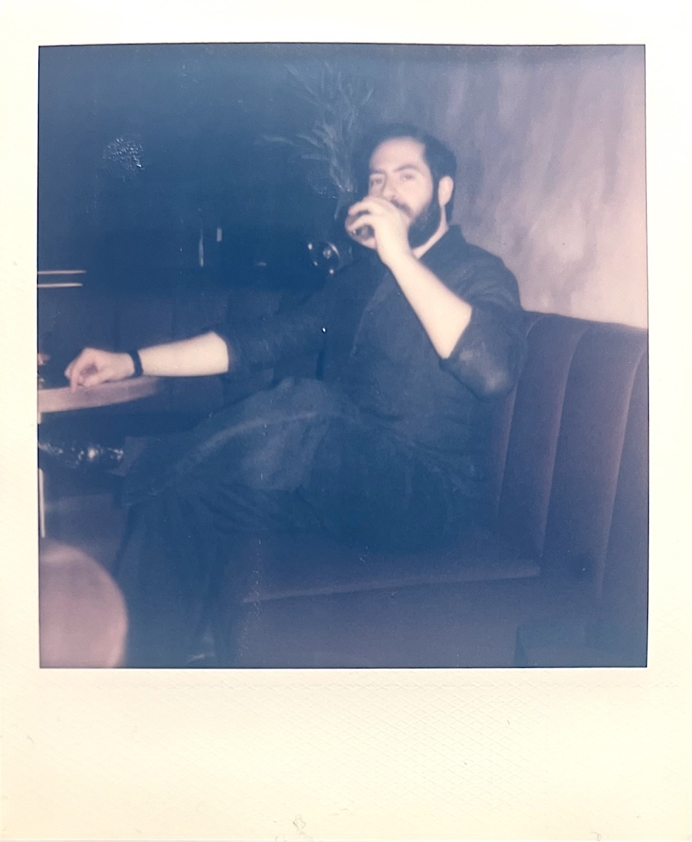 Instant-film photo of Tyler in a dim bar booth, drink in hand