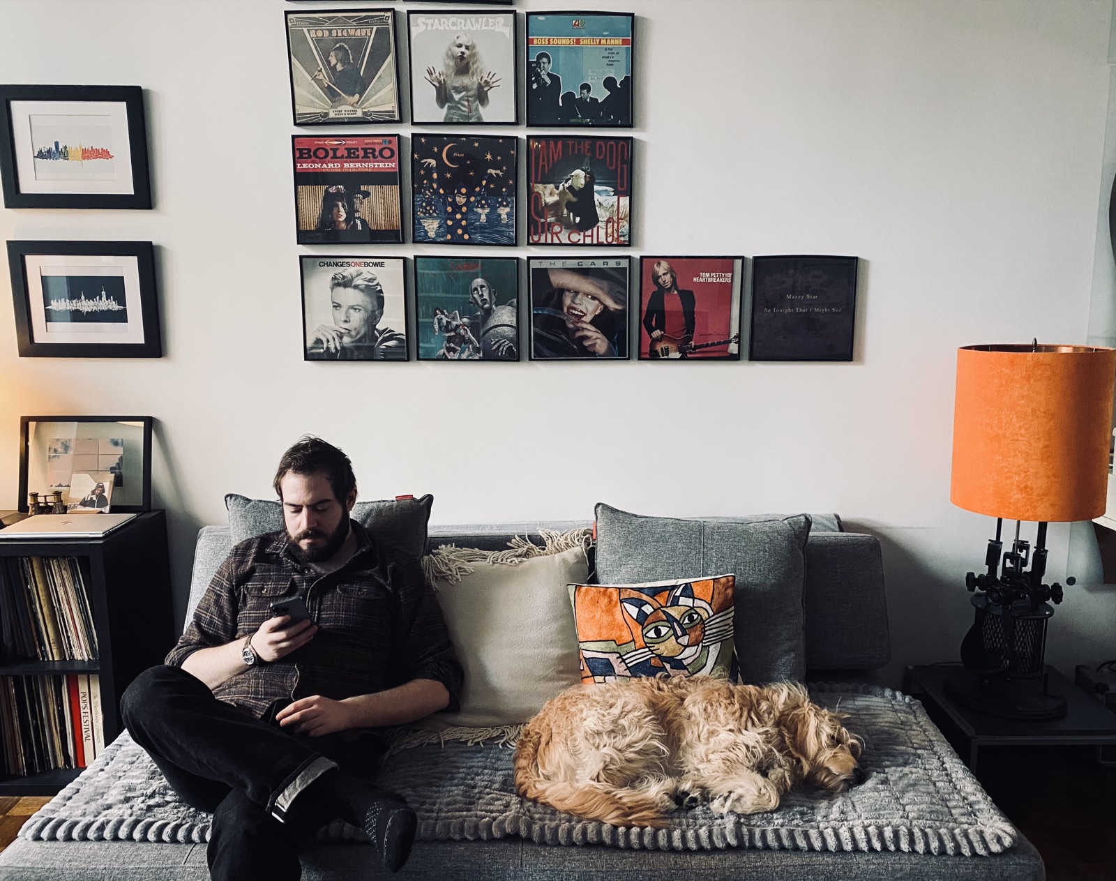 Tyler on the couch beneath a wall of framed vinyl records, with a sleeping dog beside him